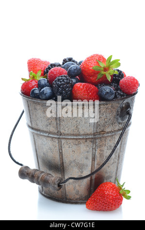 Assorted fresh picked berries in a pail with a wooden handle over a white background. Vertical format with reflection. Stock Photo