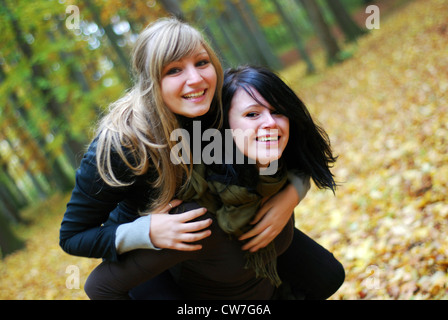 two girlfriends in the forest, one piggybacking the other Stock Photo