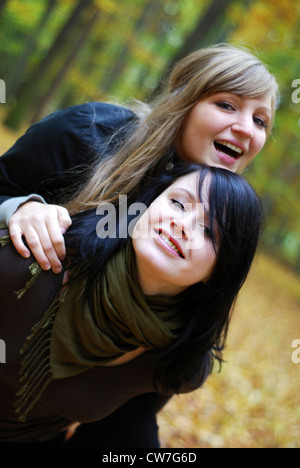 two girlfriends in the forest, one piggybacking the other Stock Photo