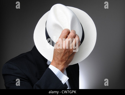 Man in a tuxedo hiding behind his hat. Horizontal closeup over a gray background. Stock Photo