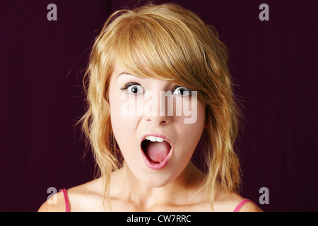 Very surprised or shocked young blond teenager girl making funny face, with eyes and mouth wide open, studio shot. Stock Photo