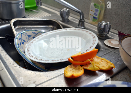 dirty sink full of dishes, bowls, cups and orange peels. Stock Photo
