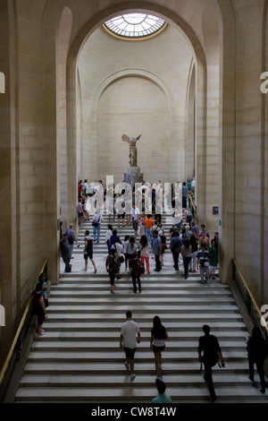 Tourists walk towards The Winged Victory of Samothrace, also called the Nike of Samothrace, a 2nd century BC marble sculpture of the Greek goddess Nike (Victory). Since 1884, it has been prominently displayed at the Louvre and is one of the most celebrated sculptures in the world. Stock Photo