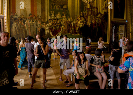 Tourists admire the Coronation of Napoleon in Coronation room of the King's apartments in the Palace of Versaille, near Paris. The painting (Le Sacre de Napoléon) is a work of almost 10 x 6 metres completed in 1807 by Jacques-Louis David, the official painter of Napoleon. The crowning and the coronation took place at Notre-Dame de Paris, a way for Napoleon to make it clear that he was a son of the Revolution. Stock Photo