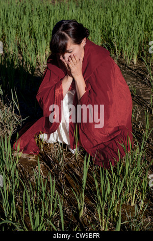 a woman in a red cape sits on a field desperately Stock Photo