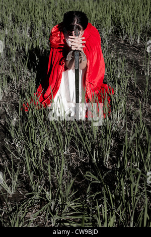 a woman in a red cloak sitting on a box with a sword Stock Photo