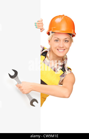Female construction worker holding a wrench, standing behind white panel Stock Photo