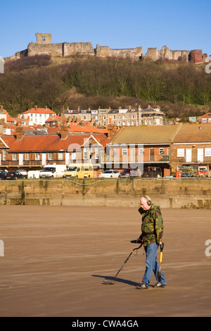 Man metal detecting on North Bay beach against the backdrop of Scarborough Castle,  Scarborough, North Yorkshire, UK Stock Photo