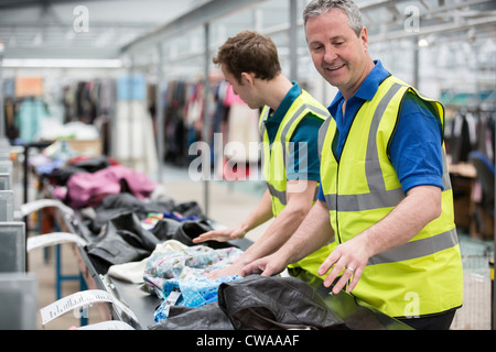 Two men sorting clothes on conveyor belt in warehouse Stock Photo