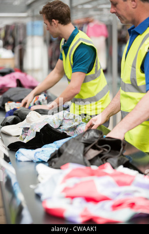 Two men in warehouse sorting clothing on conveyor belt Stock Photo