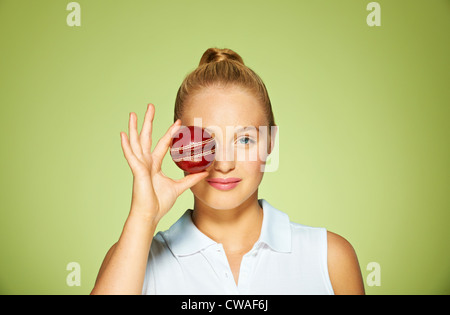 Young woman holding cricket ball over her eye Stock Photo