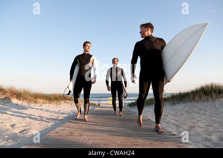 Three surfers walking on boardwalk Stock Photo
