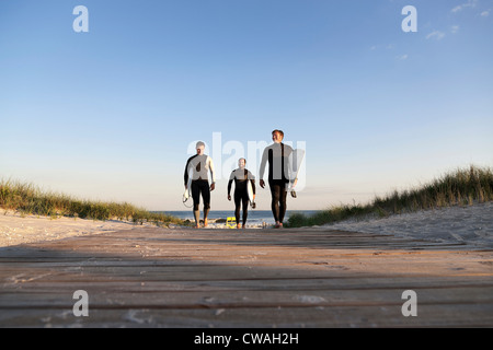 Three surfers walking on boardwalk Stock Photo