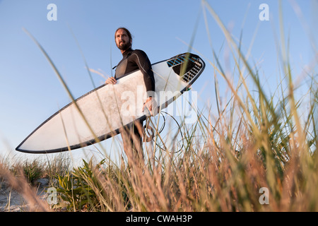 Surfer holding surfboard in grass Stock Photo