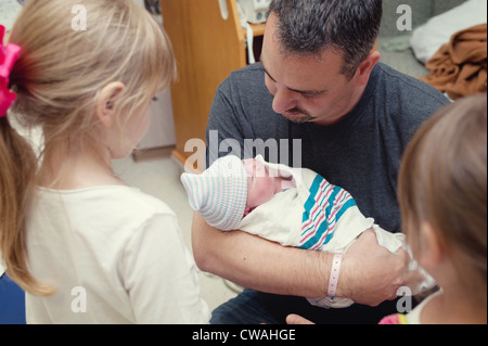 Father cradling newborn baby girl with two older sisters Stock Photo