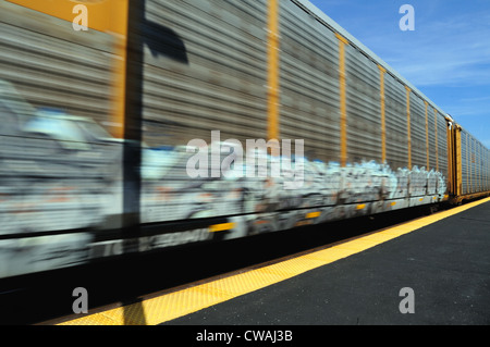 Train of auto rack carriers blur of motion through Geneva, Illinois on its way westbound from Chicago. Geneva, Illinois, USA. Stock Photo