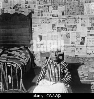 Elderly former slave in her sitting in her news papered home in May 1941. The beds are covered with handmade quilts. Stock Photo