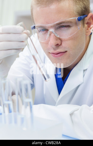 A male medical or scientific researcher or doctor looking at a test tube of clear liquid in a laboratory with microscopes. Stock Photo