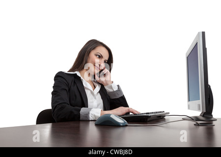 Image of a young brunette woman working on a computer and using a mobile phone , isolated against a white background. Stock Photo