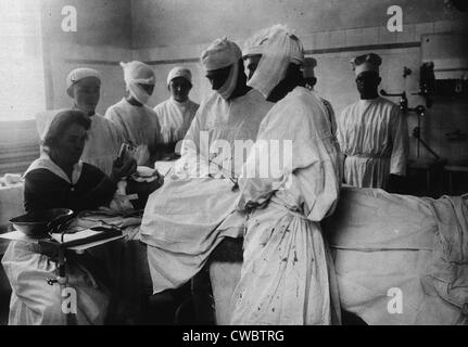 Masked surgeons perform an operation while a nurse administers ether to anesthetize patient. Ca. 1920. Stock Photo