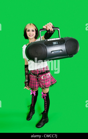 Portrait of young woman holding boom box over green background Stock Photo