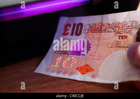 Checking 10 pound note under UV light Stock Photo