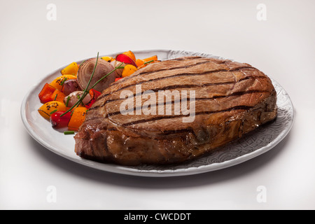 A plated, grilled rib-eye beef steak with scallion andyellow and red pepper garnish. Stock Photo