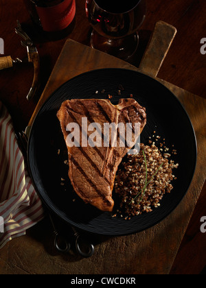 A grilled t-bone steak plated with quinoa grains and red wine. Stock Photo