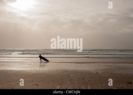 Surfer walking on beach in the evening sun at Watergate Bay near Newquay, Cornwall, UK Stock Photo