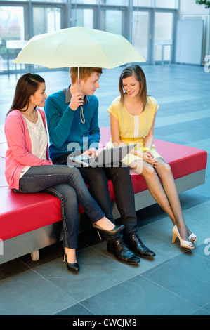 Male business executive using a laptop with his female colleagues and holding an umbrella Stock Photo