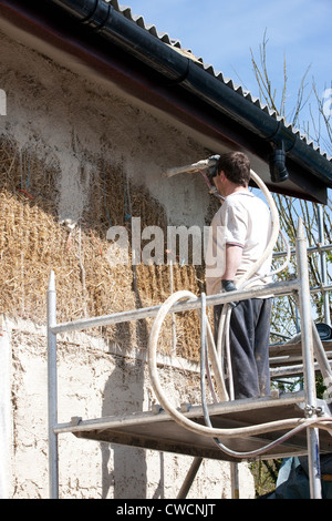 Render being applied to a straw covered building Stock Photo