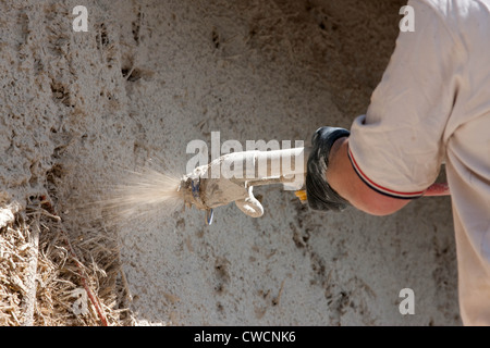 Render being applied to a straw covered building Stock Photo