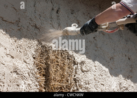 Render being applied to a straw covered building Stock Photo