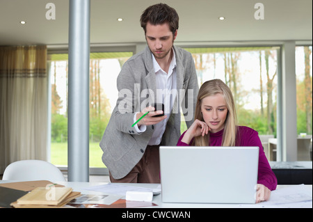 Woman working on a laptop with a man using mobile phone beside her Stock Photo