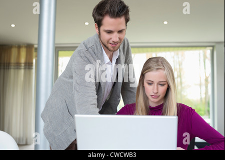 Woman working on a laptop with a man standing beside her Stock Photo