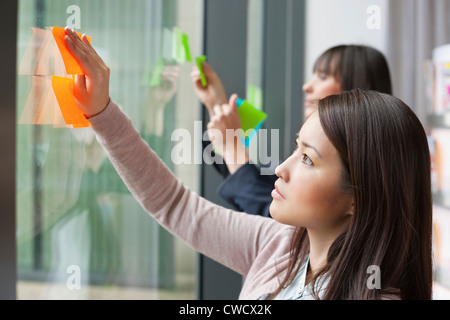 Businesswomen sticking memo notes on glass in an office Stock Photo