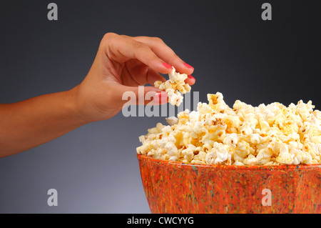 Closeup of a womans hand taking some popcorn from a bowl. Horizontal format over a light to dark gray background. Stock Photo