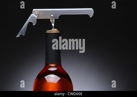 Closeup of a metal waiters corkscrew in a red wine bottle. Horizontal format over a light to dark gray background. Stock Photo