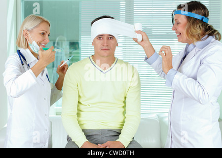Portrait of two careful female doctors giving first aid to male patient in hospital Stock Photo