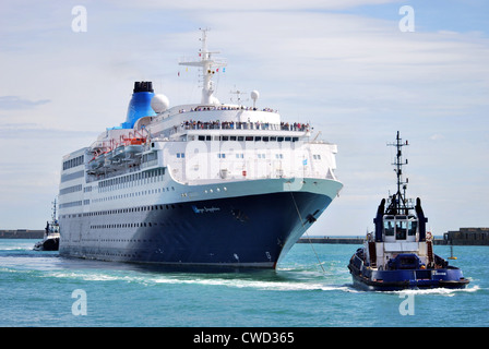 The cruise ship Saga Sapphire arrives in Dover during the day and is assisted past the Prince of Wales pier by the harbour tugs Stock Photo