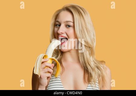 Portrait of a beautiful blond woman eating banana over colored background Stock Photo