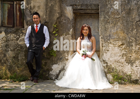 Horizontal portrait of a beautiful Vietnamese bride and handsome groom posing for photographs by a derelict building in Vietnam. Stock Photo