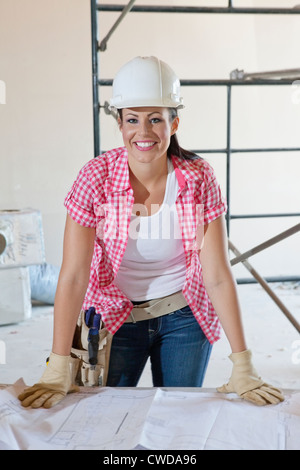 Portrait of a happy female construction worker wearing hardhat with blueprints Stock Photo