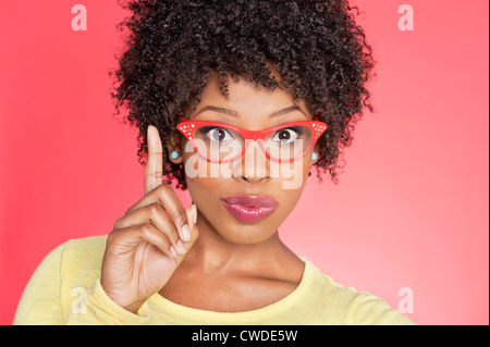 Portrait of an African American woman in retro glasses pointing upward over colored background Stock Photo