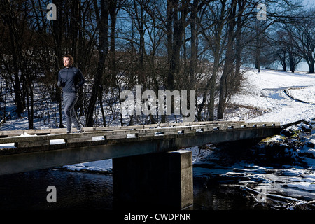 A man runs on a bridge over a creek in the snow. Stock Photo