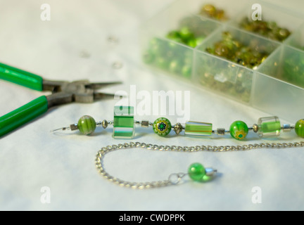 Beautiful apple and sage green artisan necklace waits atop a jeweler's work bench, in a middle stage of assembly. Stock Photo