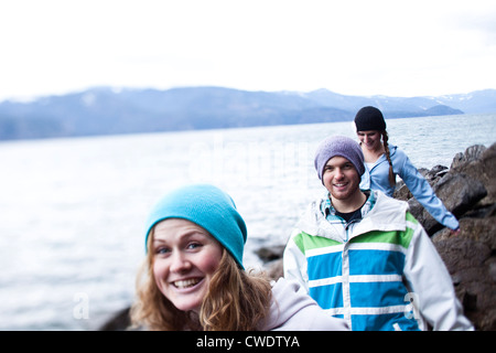 A group of three young adults smile while hiking at the edge of a lake in Idaho. Stock Photo