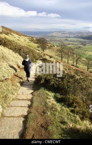 A woman walking down a paved path down from Mam Tor, a hill near Castleton in the High Peak of Derbyshire, Peak District National Park, England, UK Stock Photo
