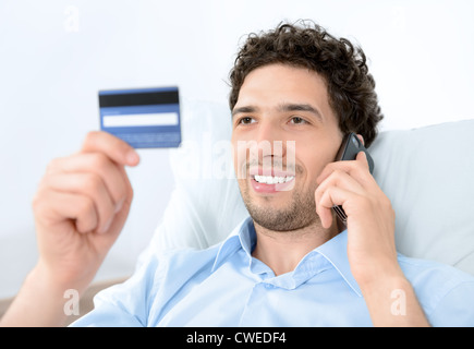 Young handsome man looking on credit card and talking on modern mobile phone. Studio shot. Stock Photo