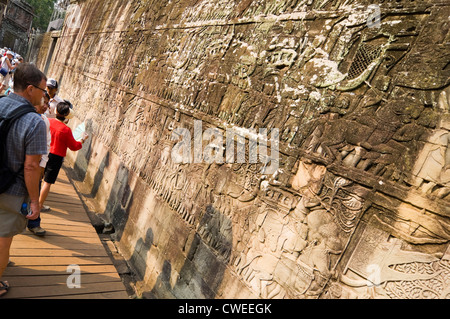 Horizontal close up view of tourists looking at the historical bas-reliefs in the outer gallery of the Bayon temple at Siem Reap Stock Photo